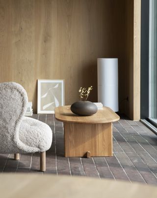 A boucle chair alongside a wooden coffee table with a potted plant