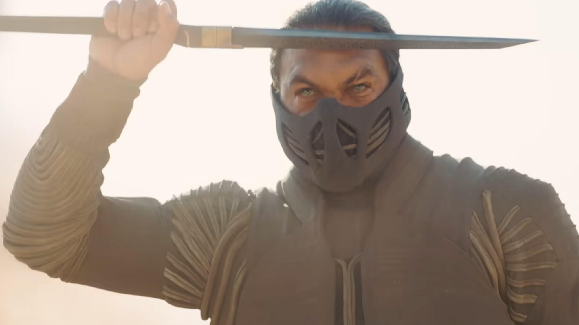 Jason Momoa wearing a mask and holding a sword to his forehead.