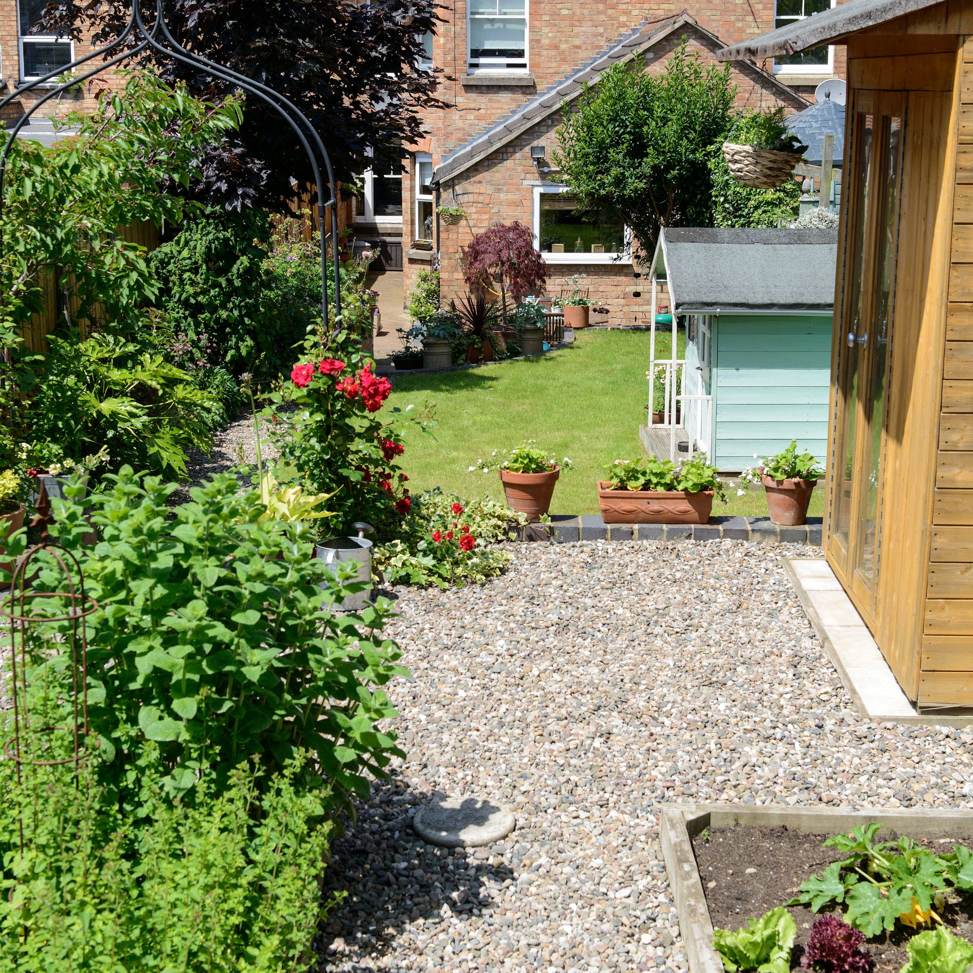 Gravel garden in front of grass lawn with potted plants and Wendy house