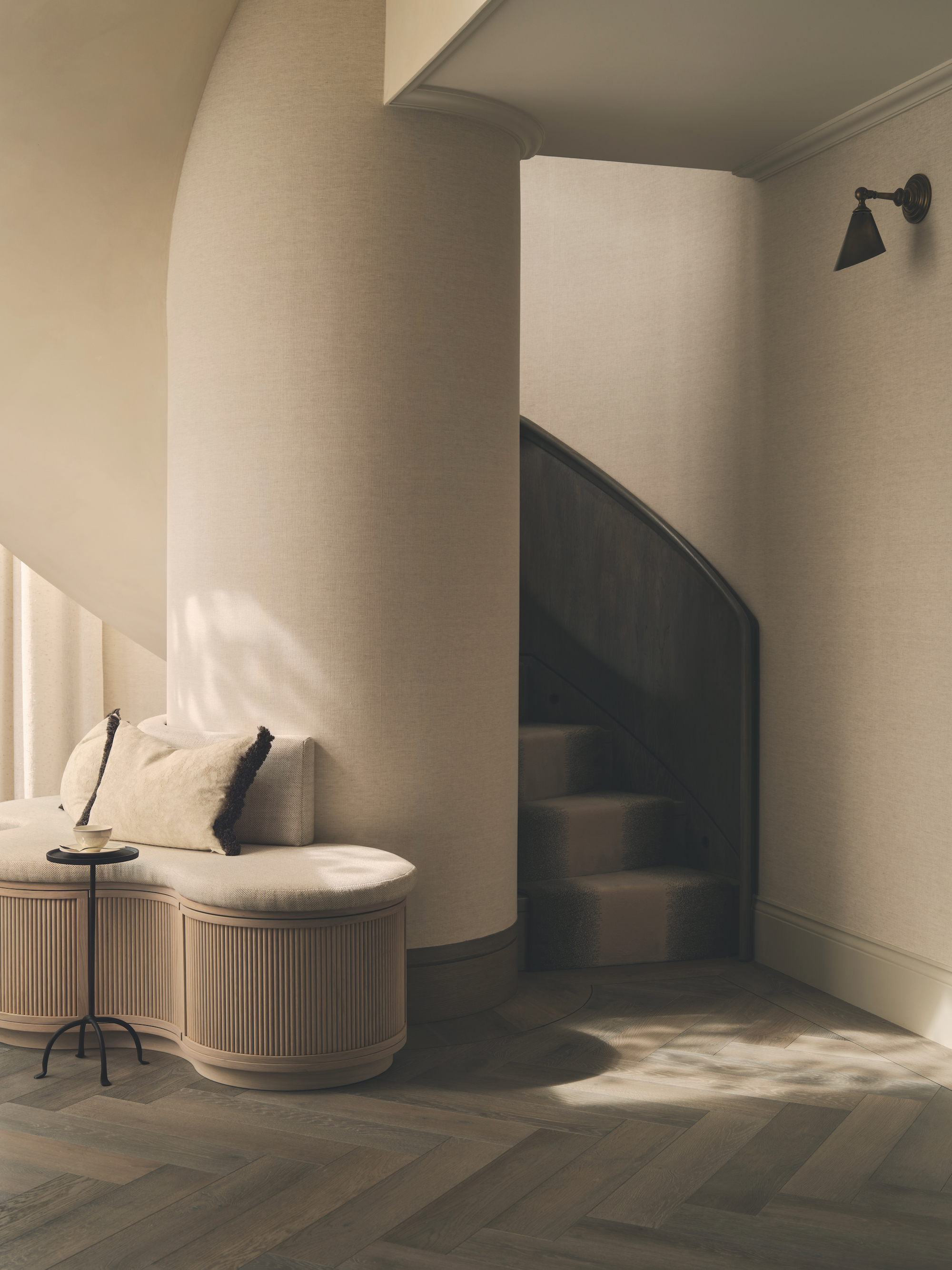 A neutral tones entryway with a carpeted spiral staircase and a small curved bench seats to the left.
