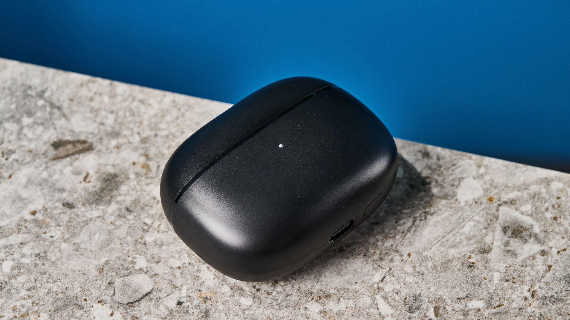 a pair of black and silver earbuds with silicone tips and a black charging case are photographed against a blue background