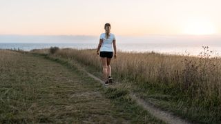 Woman wearing shorts and t-shirt power walking down path next to seafront