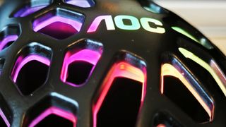 A black AOC GM510 gaming mouse with a hollow honeycomb structure and RGB lighting sitting on a desk