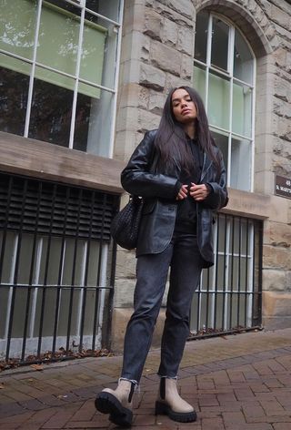 best black jeans is shown on a woman standing on the sidewalk wearing a black leather jacket over a black sweater and black skinny jeans and tan chelsea boots