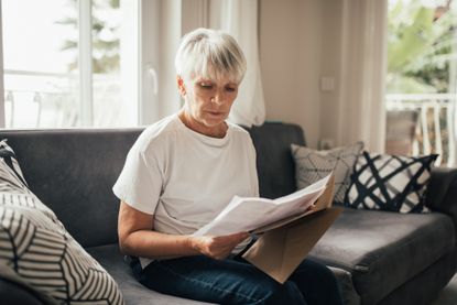 Elderly woman received mail with invoices, utility bills, credit payments or bank statement. She serious and concentrated. Paperwork at home. Household routine and chores.