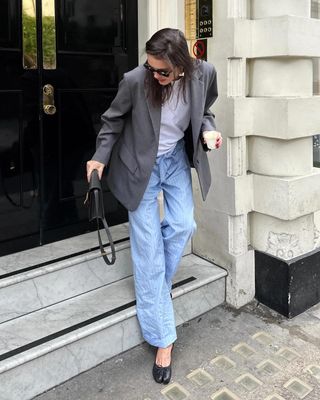 British fashion influencer Valeria Sobalera poses on a London sidewalk wearing a gray blazer, white T-shirt, striped blue pajama pants, and black Margiela ballet flats.