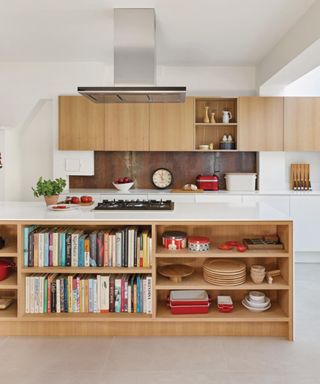 A view across a kitchen island in the kitchen diner with white flooring and white and wood kitchen units with books and cookware on them