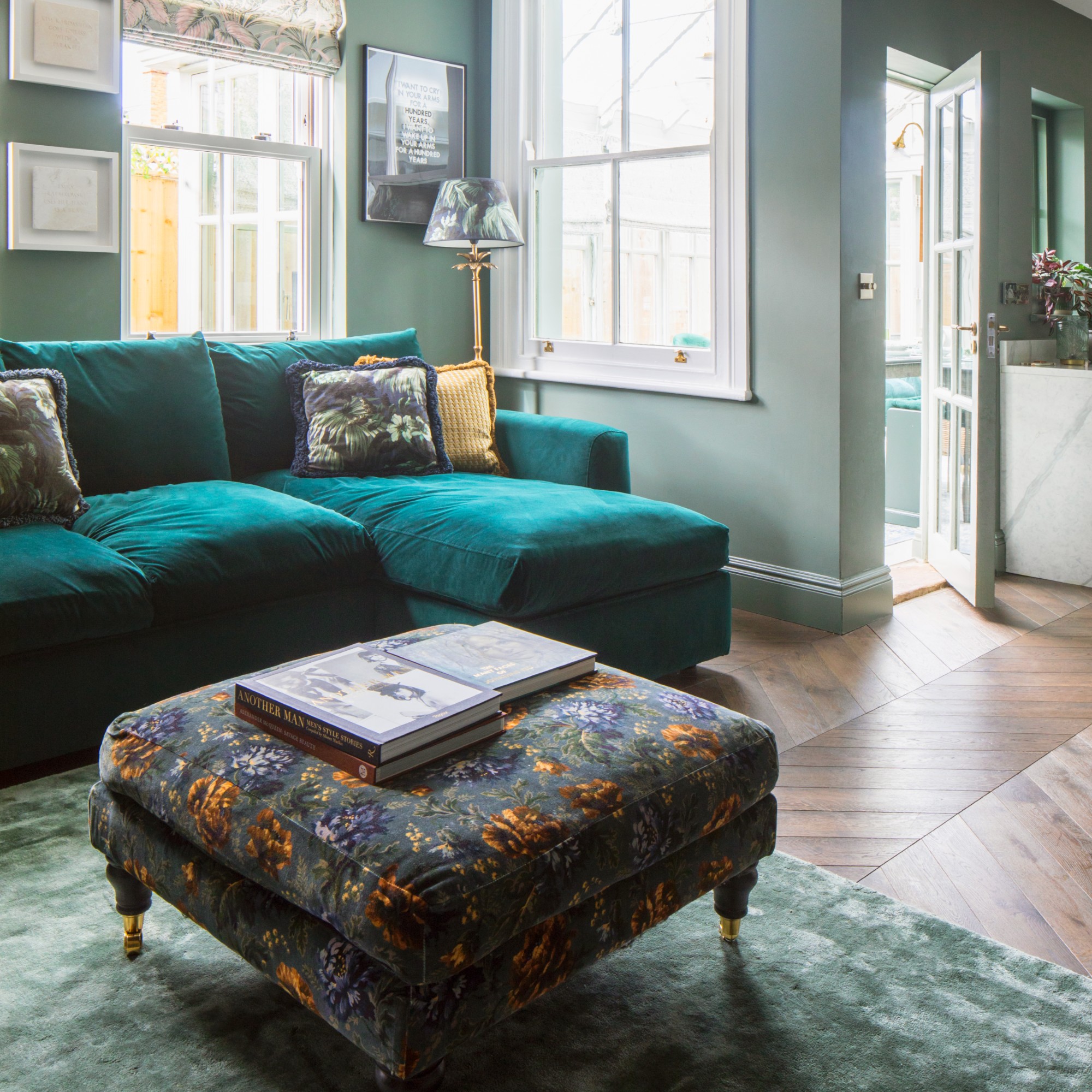 A sage green-painted living room with a chaise emerald green velvet sofa