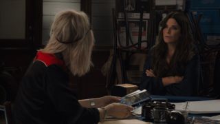 Sandra Bullock looking at Cate Blanchett with her arms crossed and a serious expression in Ocean's 8.