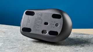 A photo of the Logitech MX Anywhere 3S mouse upturned on a stone surface with a blue wall in the background.