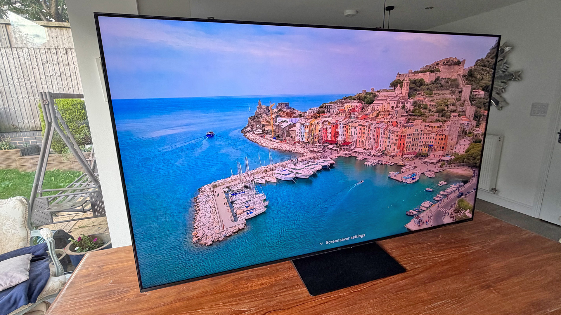 TCL C7L Mini LED TV on wooden table, on screen is panoramic view of seaside town