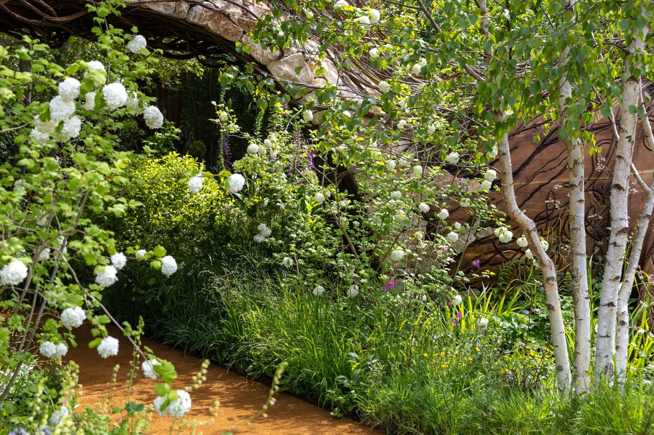 Images of the CPRE Show Garden On the Edge by Sarah Eberle. it focuses on grasses and flowers that grow around britain's edges, and is centred around a giant wooden carving of Gaia
