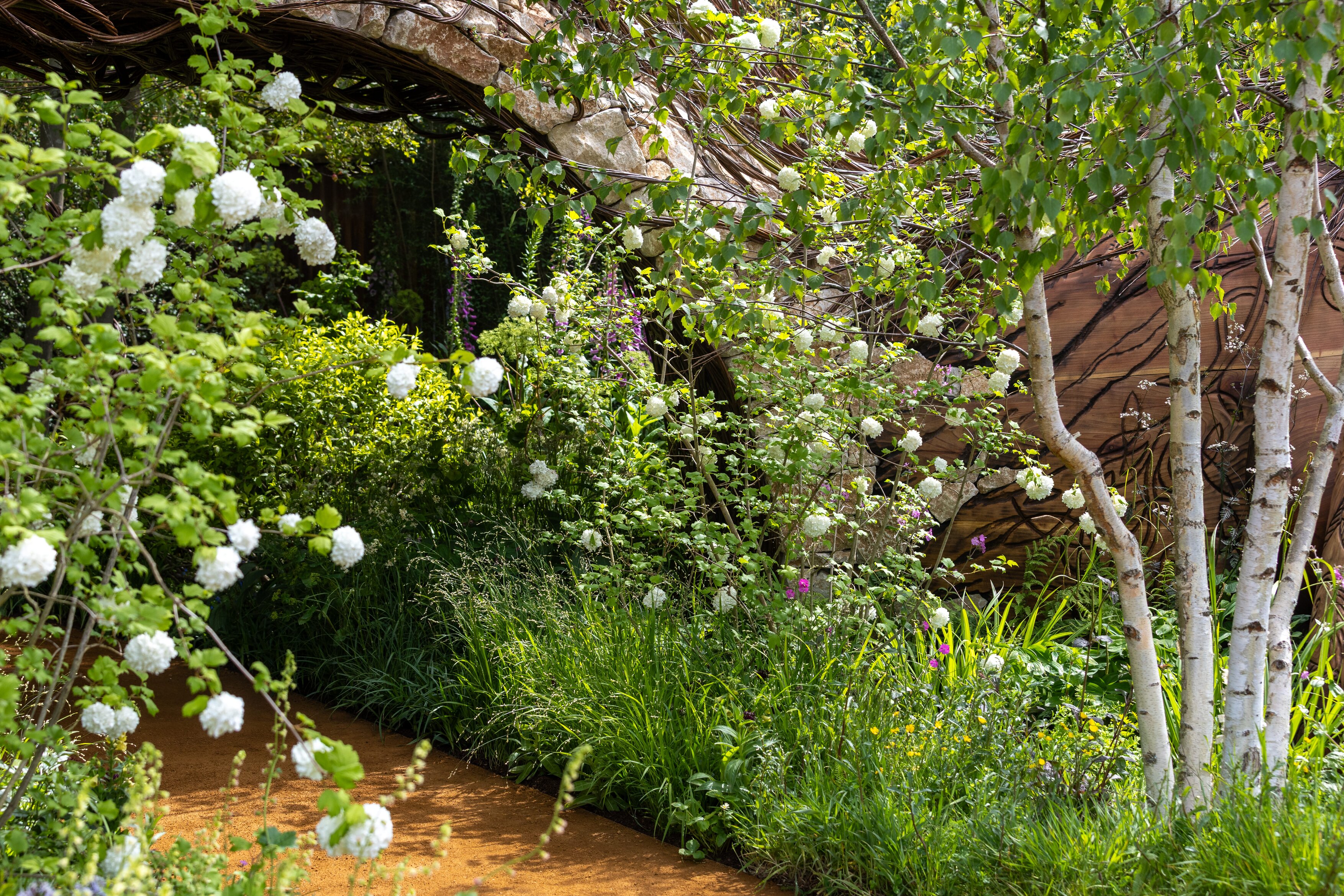 Images of the CPRE Show Garden On the Edge by Sarah Eberle. it focuses on grasses and flowers that grow around britain's edges, and is centred around a giant wooden carving of Gaia