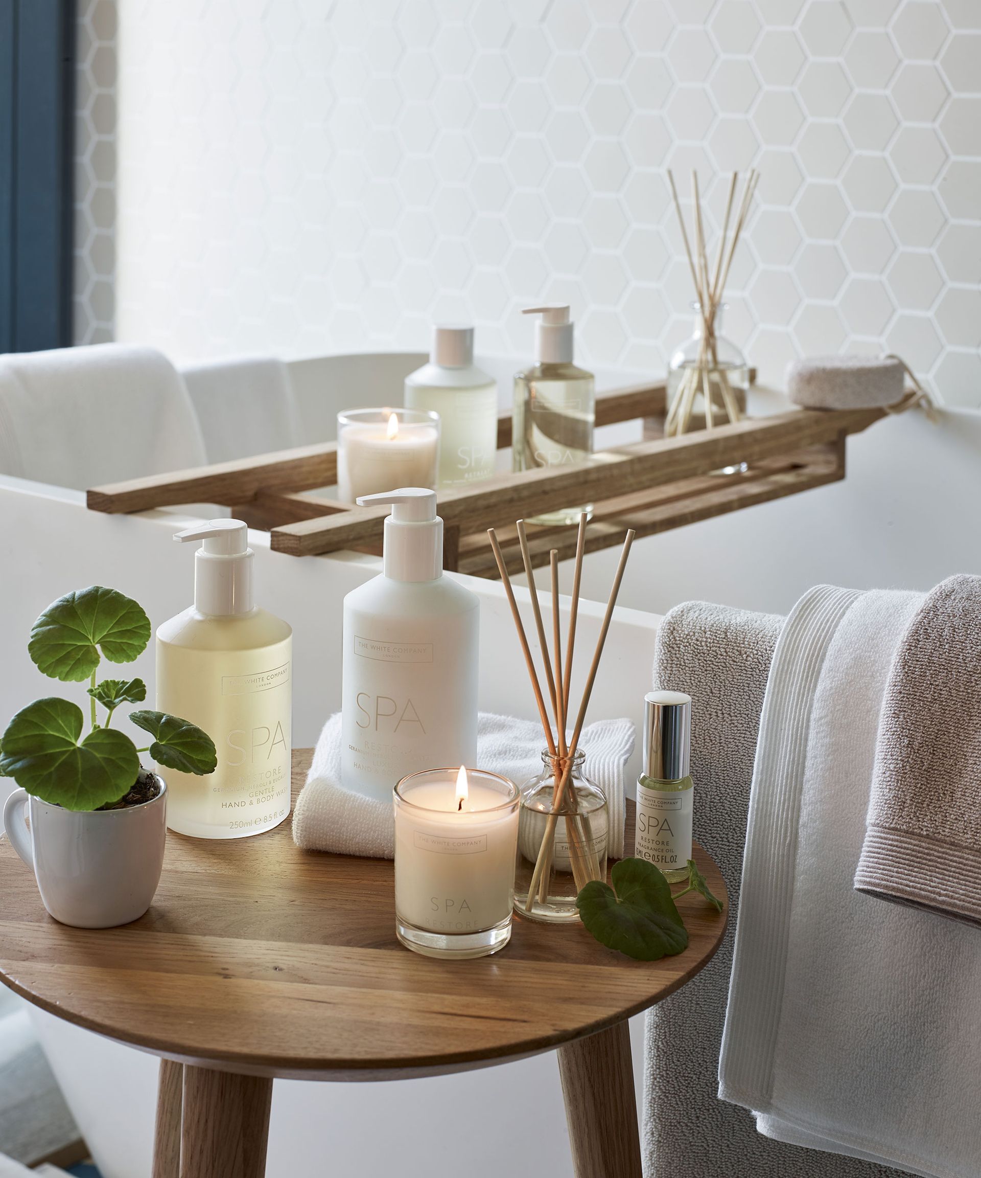 Candles, toiletries and diffusers on the bath board in the all white bathroom
