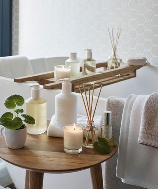 Candles, toiletries and diffusers on bath board in bathroom of all white
