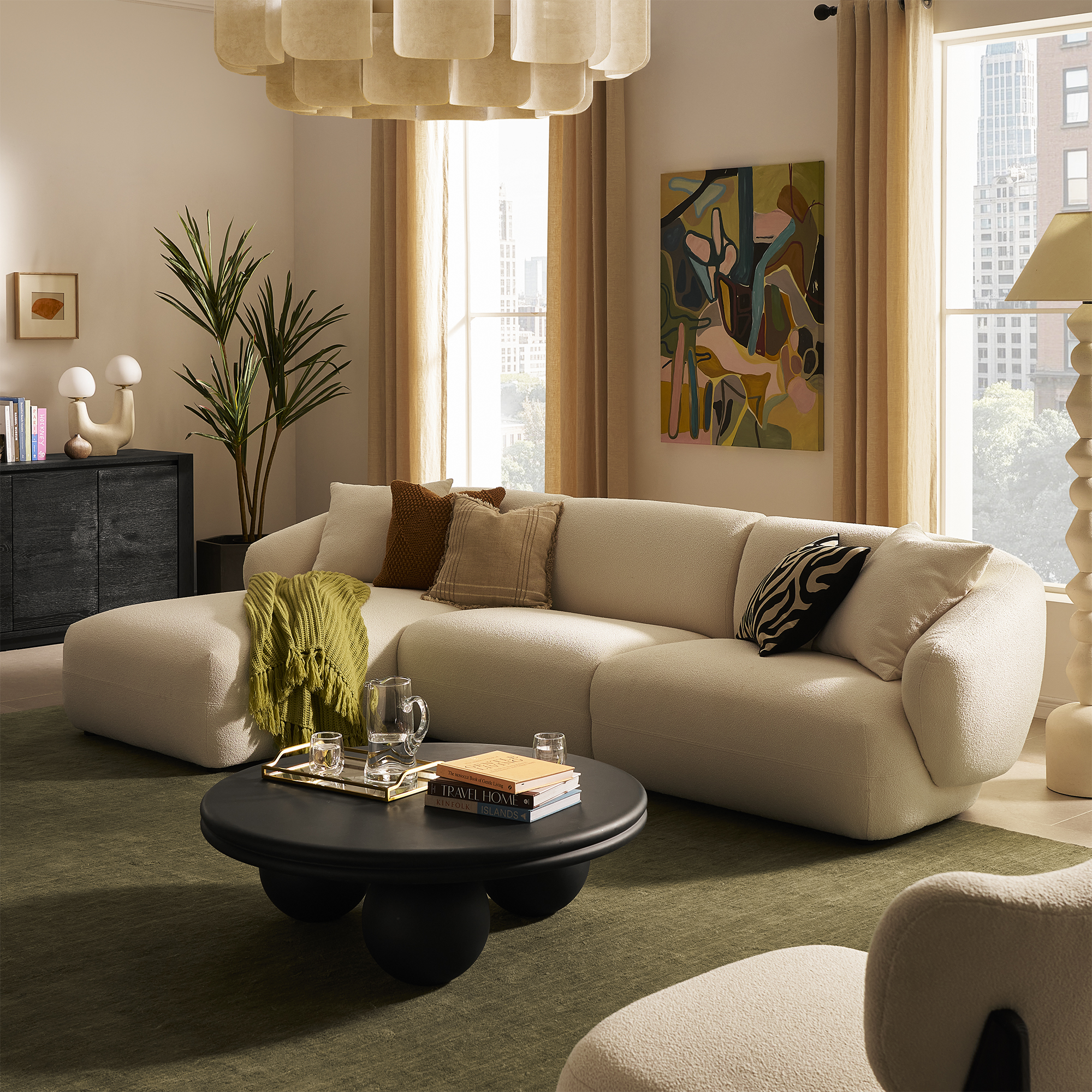 Image of a beige living room with a large white sofa and a green rug. There is a black coffee table in the center with large ball feet.