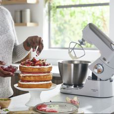 Woman making three layer cake and stand mixer on kitchen counter