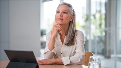 An older woman sits in an office in front of a laptop computer.