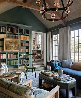 library with vaulted ceiling, statement pendant light, green bookcase, blue sofa, floral cane chairs