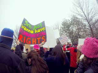 Crowds of women and men holding protest signs march through the streets during the Women's March on Washington, D.C.. Prominent sign says, "Girls Just Wanna Have Fundamental Rights." Protest. March. Community. Togetherness.