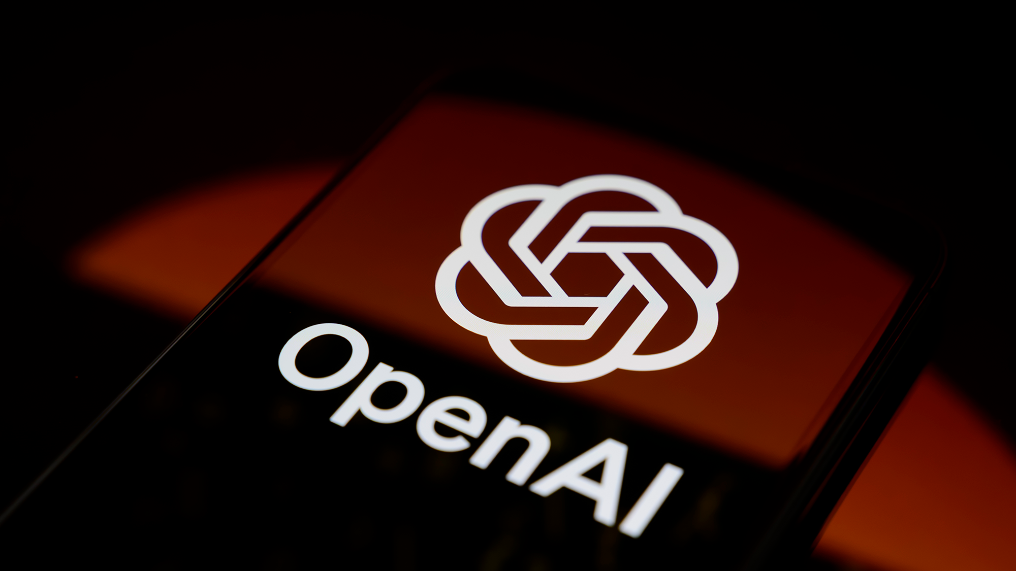A close up of a red phone screen with a white circular logo and the word "OpenAI" on the front