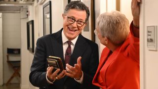 Stephen Colbert smiles while chatting with Jamie Lee Curtis behind the scenes in The Late Show with Stephen Colbert.