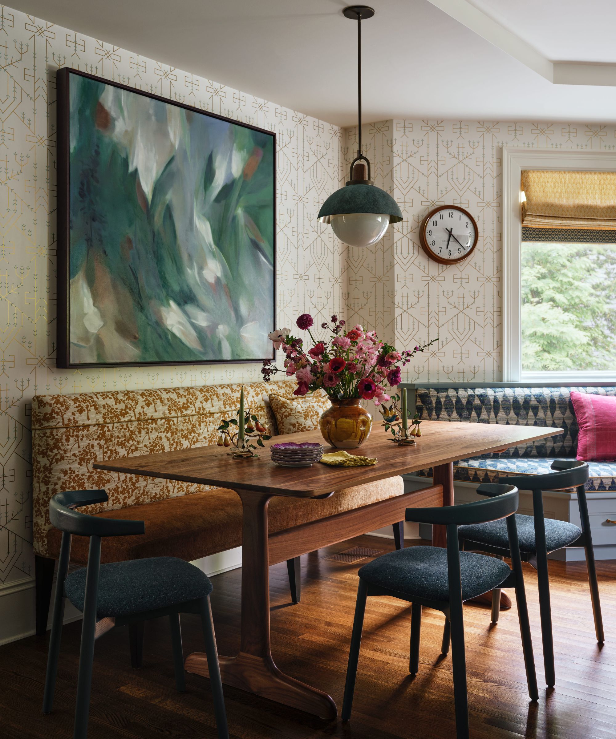 Dining nook featuring a wooden table, dark chairs, and an orange patterned bench beneath a large abstract green painting.