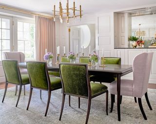 neutral dining room with paneling, brass chandelier, wooden table. green velvet chairs, lavender wing chairs and gray rug
