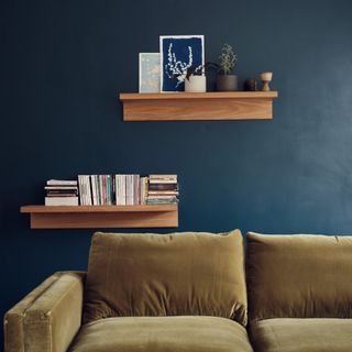 Farrow & Ball Hague Blue in a living room with floating wood shelves and a green sofa