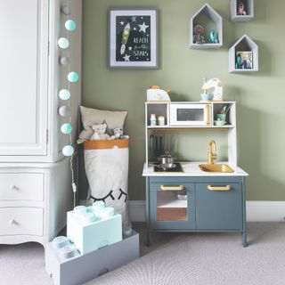 A sage green-painted kids' playroom with a toy kitchen and Lego storage