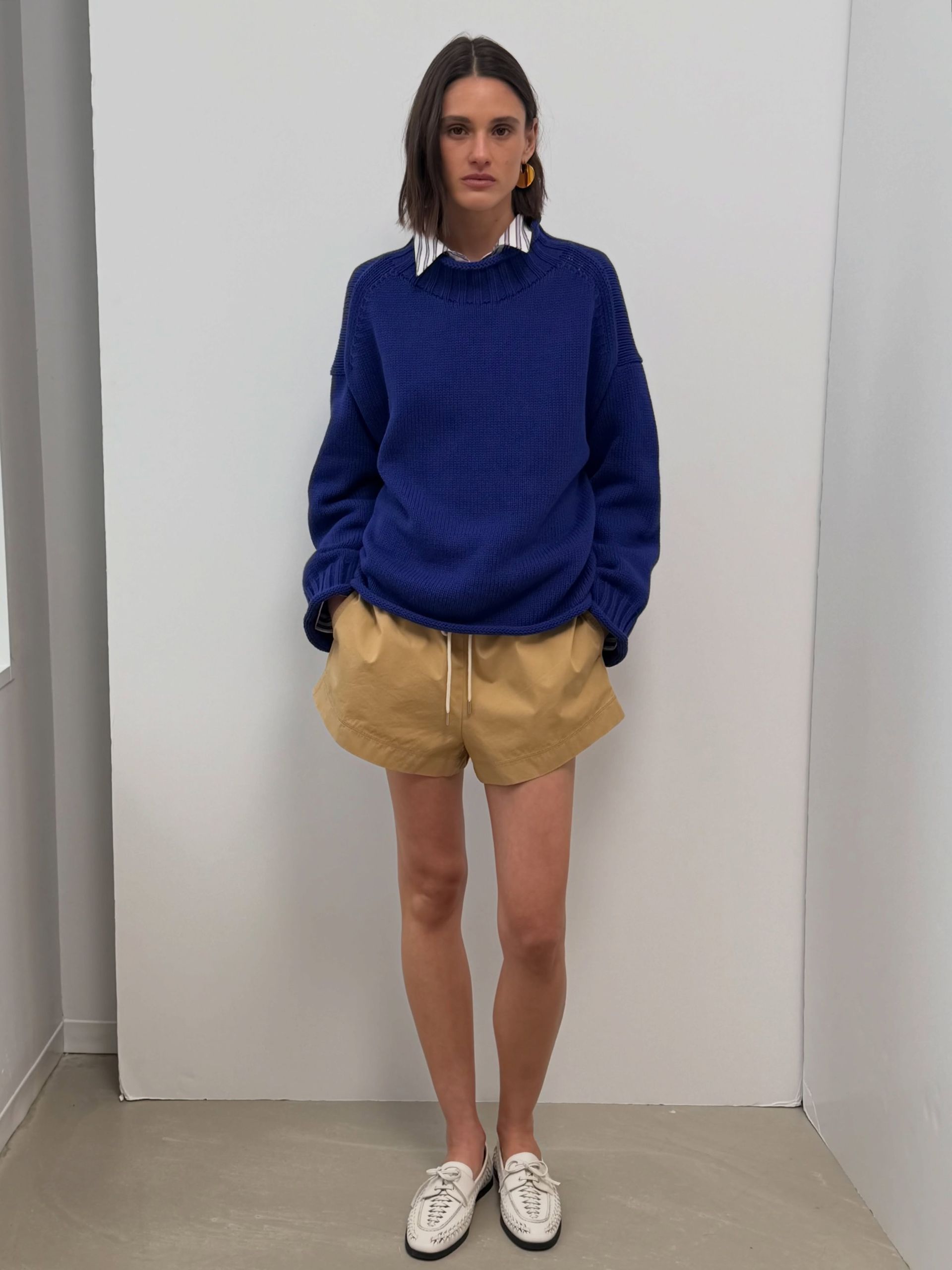 a model wears a blue sweater, khaki shorts, and white flats.