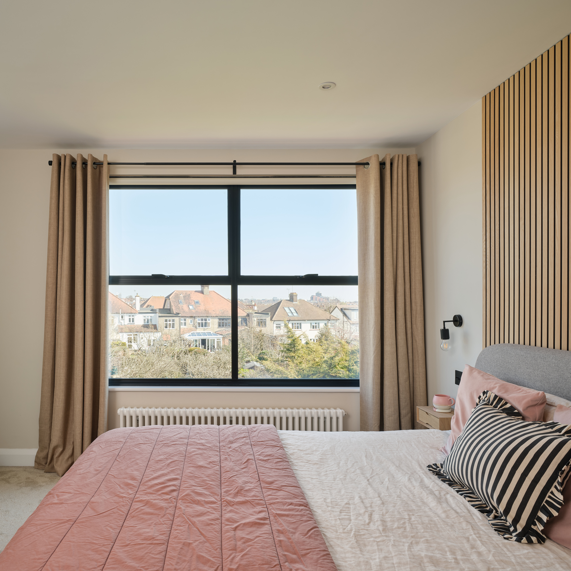 double bedroom with a large window, pale walls, pink and terracotta bedding and vertical wall panelling for a headboard