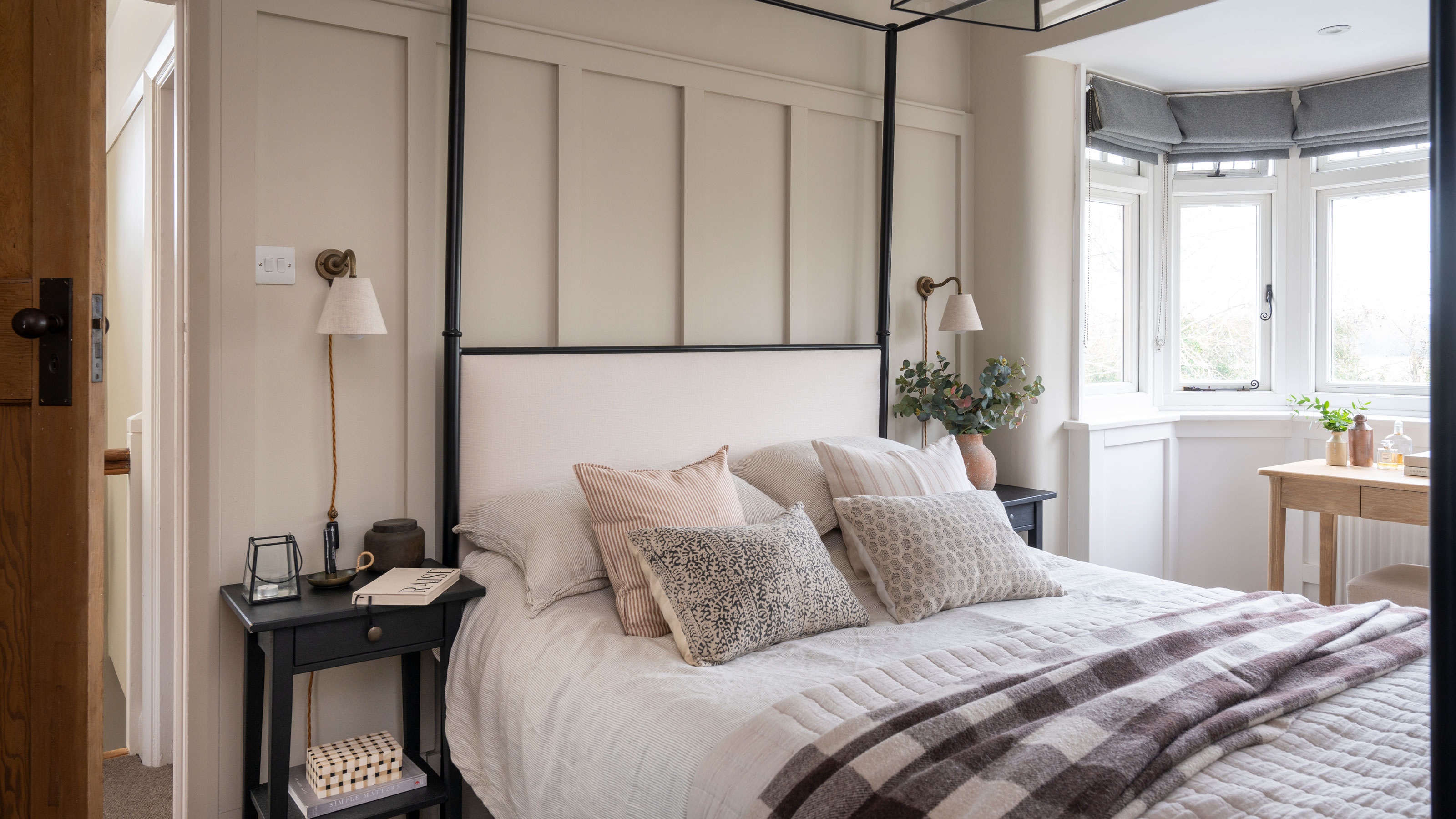 Bedroom with upholstered four poster bed, wall panelling and plug in wall lights