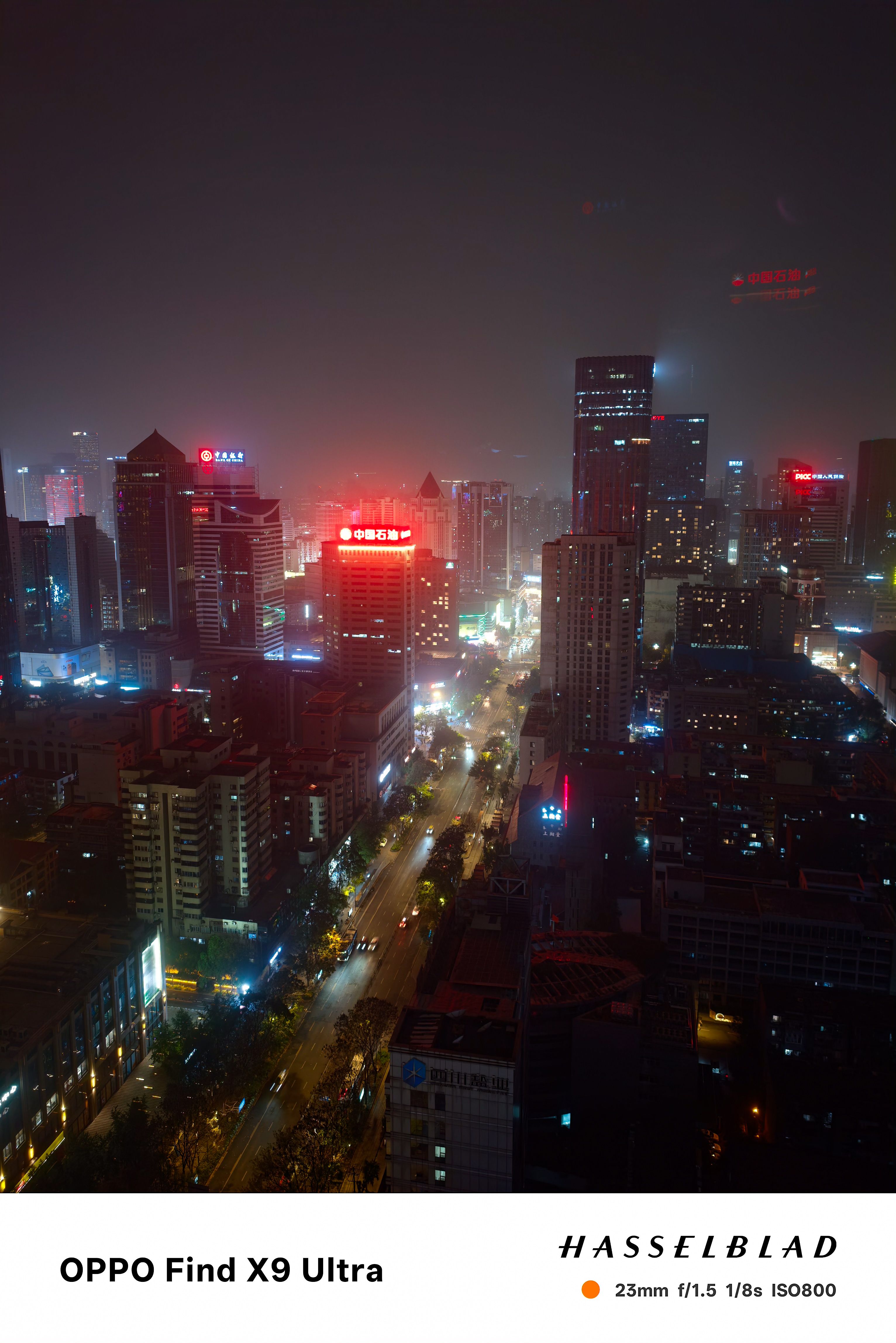Night city skyline seen from above, with glowing streets and neon-lit high-rise buildings under a hazy sky