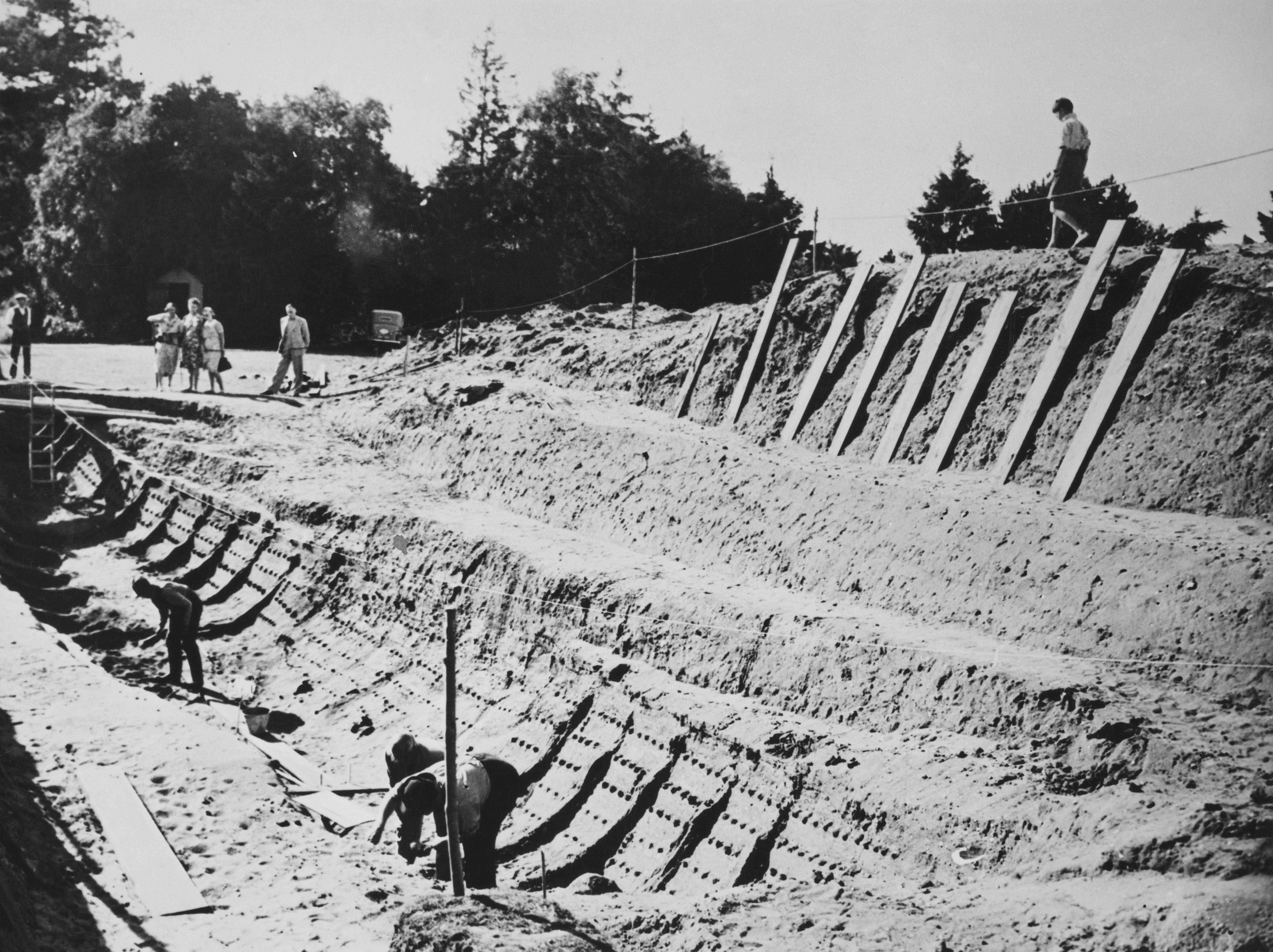 A group of people watch the excavations at the site of an Anglo-Saxon ship burial at Sutton Hoo, near Woodbridge, Suffolk, in 1939.