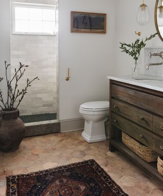 Bathroom with hexagonal tile floor and white walls and dark wood vanity with patterned bathroom rug in front