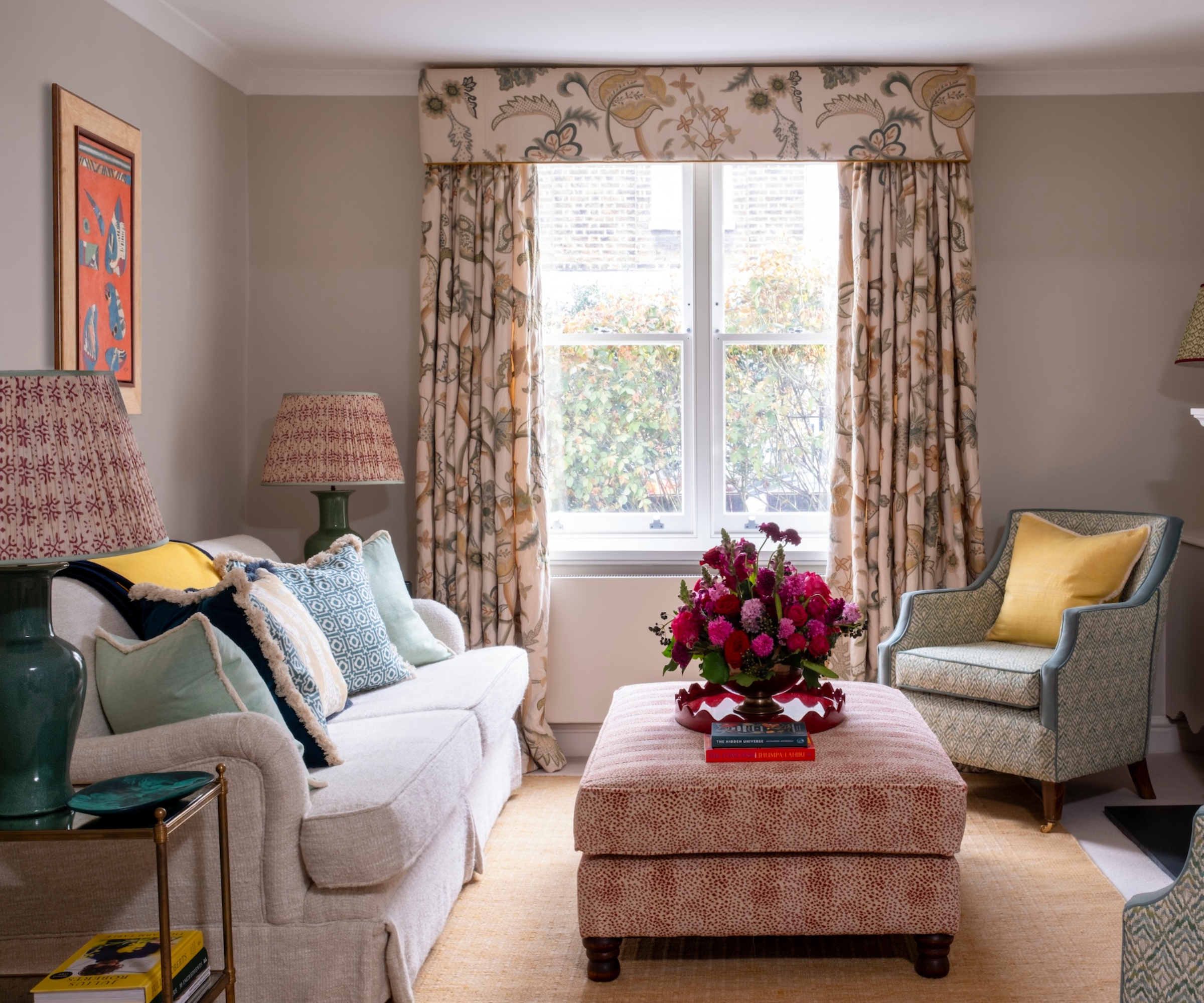 living room with cream sofa, armchairs, footstool acting as coffee table, curtains at window, side table and shelving to side of sofa