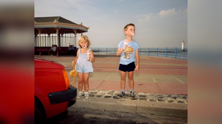TwText: A photograph of two children eating ice cream, standing beside a red car