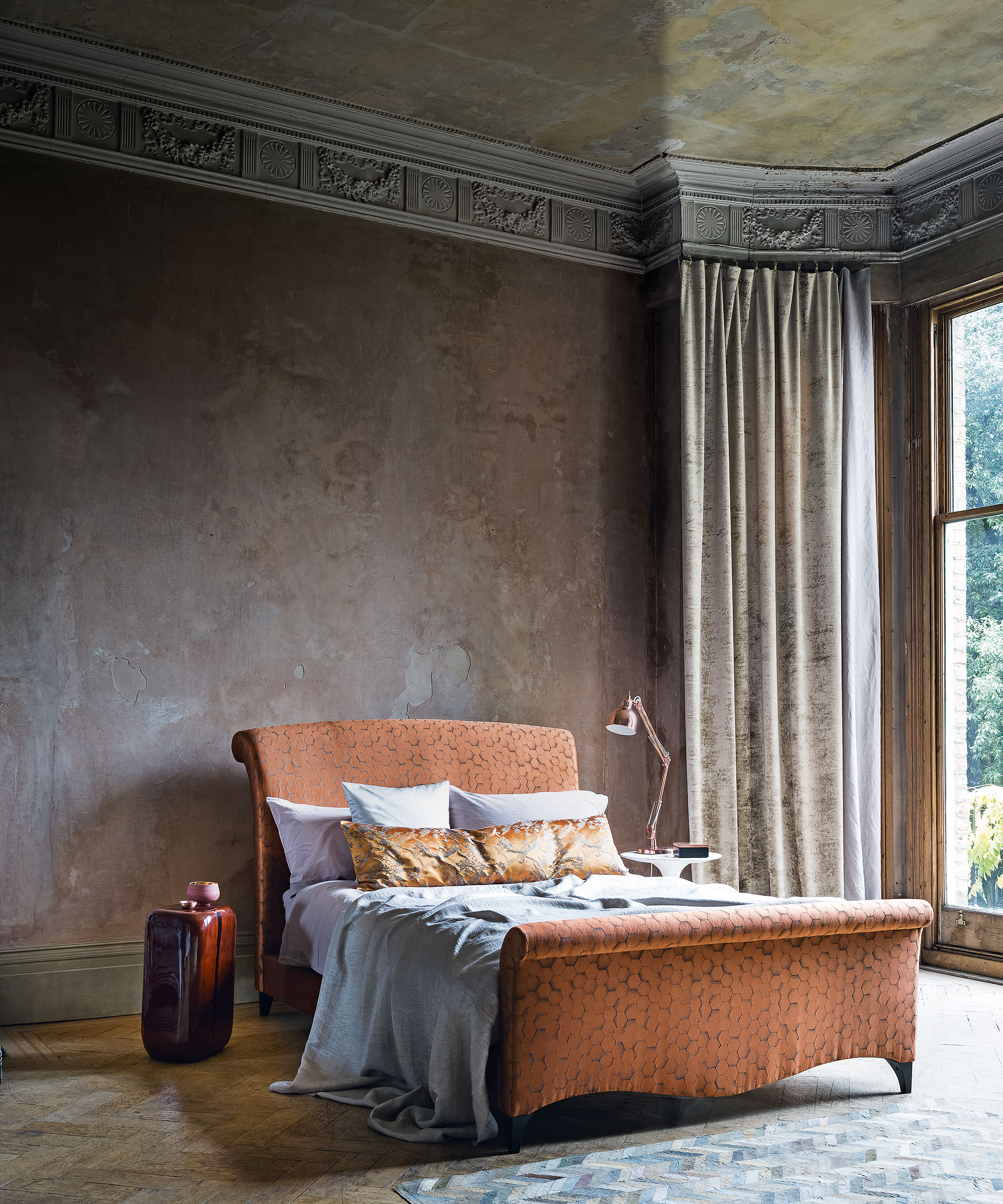 Luxury bedroom ideas with wallpapered ceiling and orange bed in front of a plaster wall.