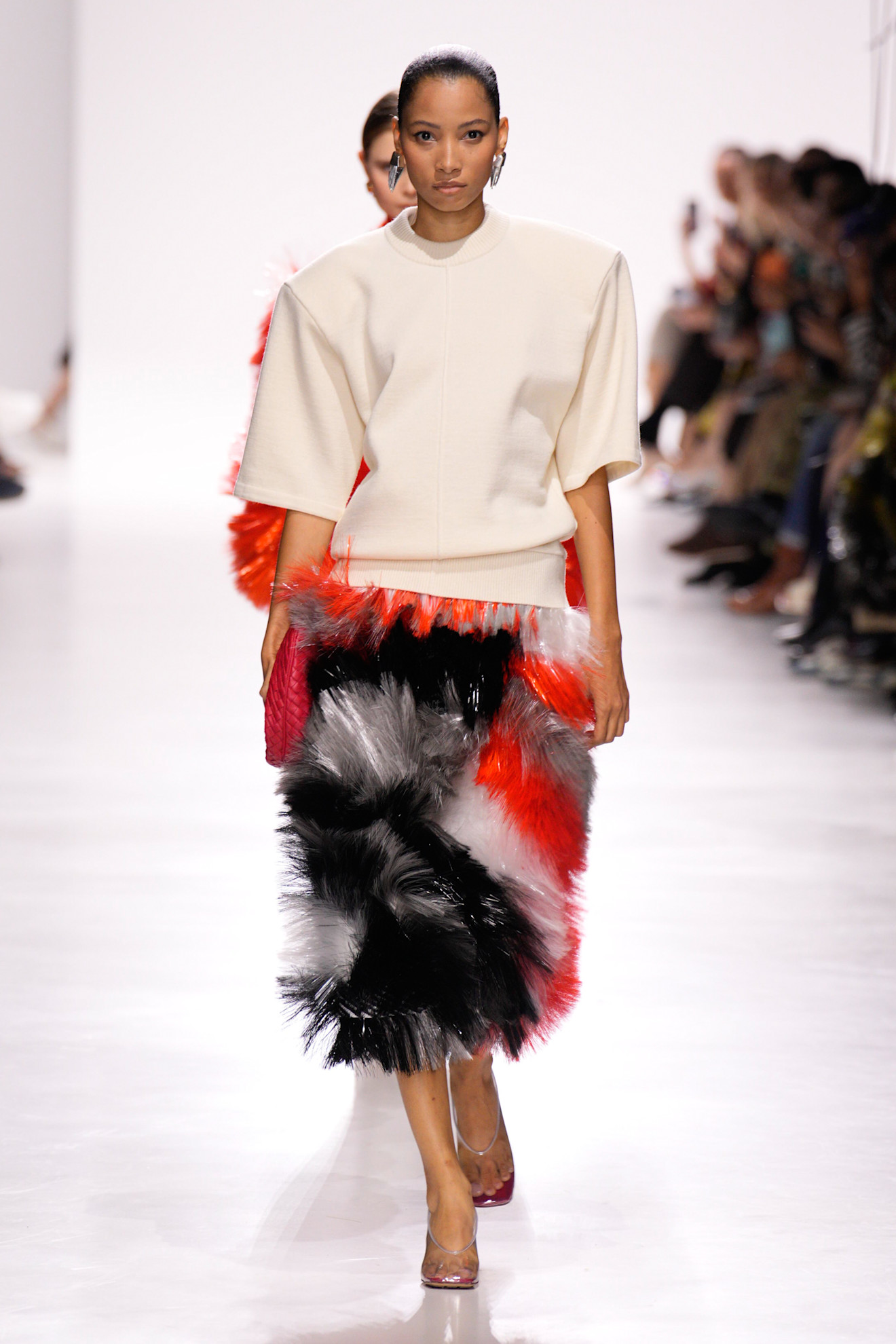 A model at the Bottega Veneta S/S 26 show wearing a shoulder-pad T-shirt with PVC pumps and a tinsel, multicolored skirt.