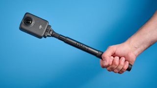 The DJI Osmo 360 on a selfie stick against a blue background