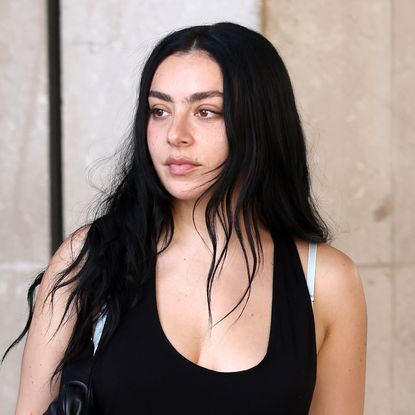 Charli XCX wears a black mini dress with pointed-toe pink crocodile pumps and has long black hair