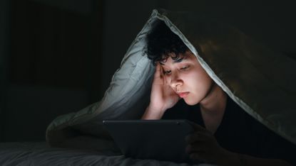 Teenage girl using smartphone in bed late at night with sad facial expression