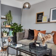 A small living room with a grey velvet sofa and glass nesting coffee tables with black metal frames