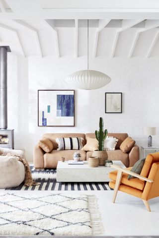 white living room with beams, sofa, armchair and rugs, pictures on wall