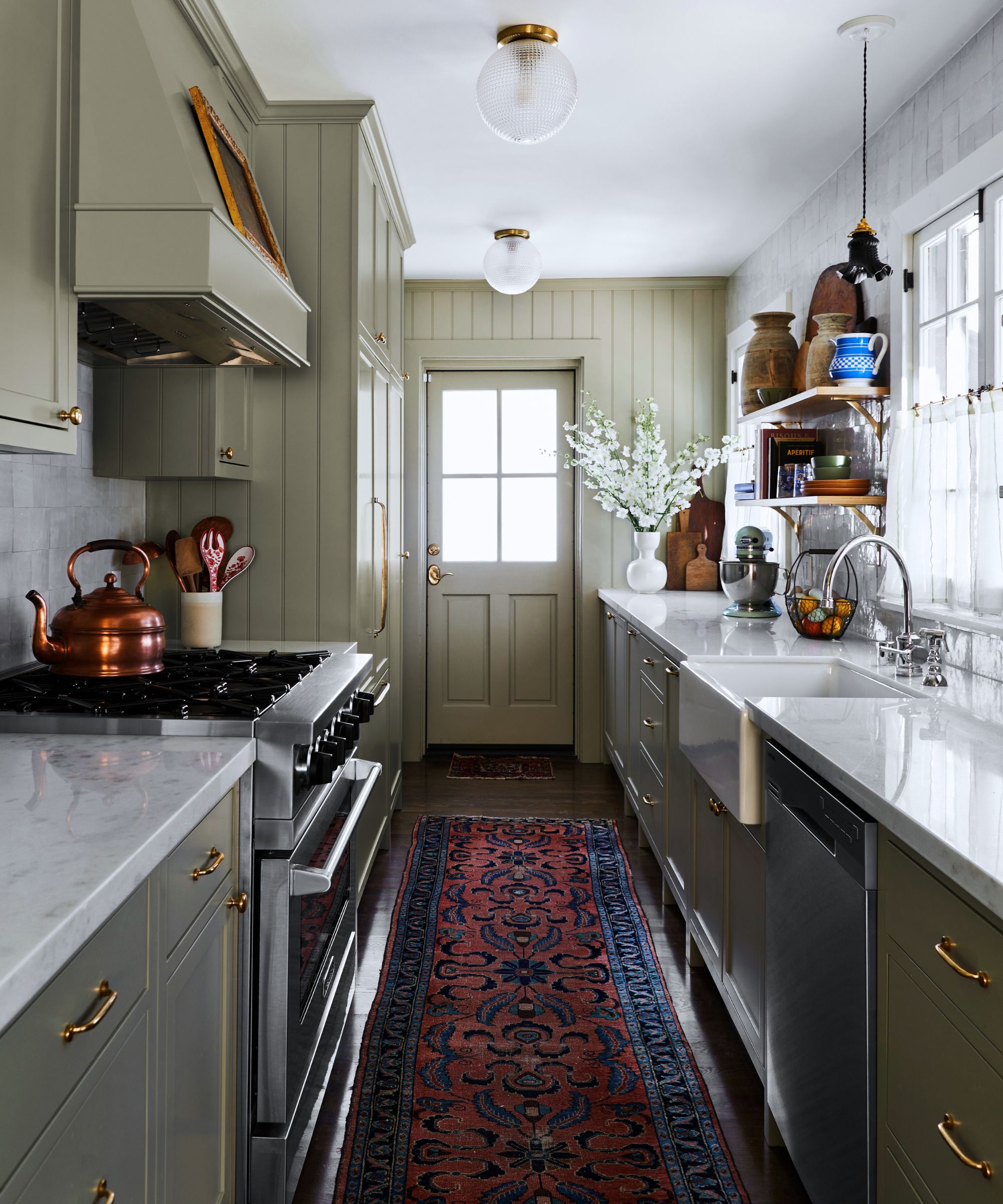 A galley kitchen with gray-green cabinets and marble countertops