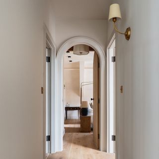 A white hallway with an arched doorway and a wall light