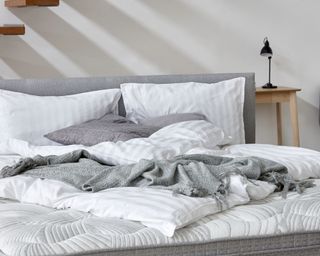 an unmade bed with grey throw in a Scandi style bedroom