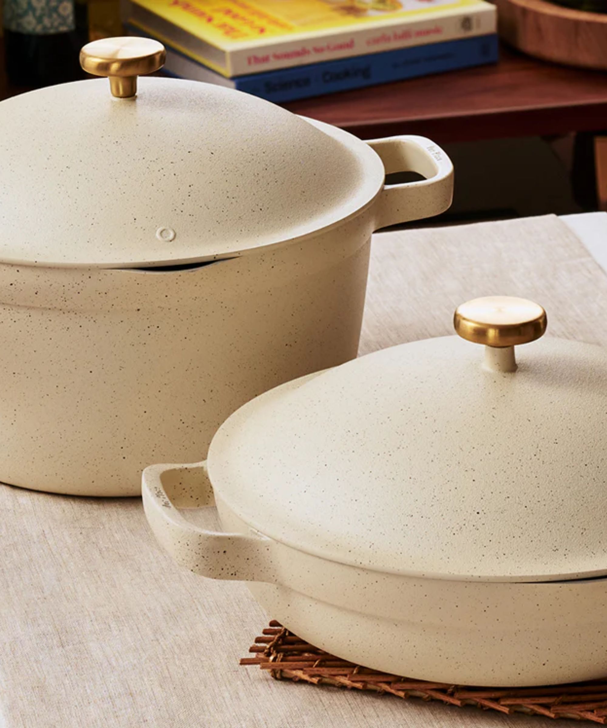 A set of two cream colored speckled pans with brass hardware on a kitchen counter