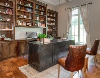 Home office with metal desk and floor to ceiling wood shelving, wood floor, rug, and neutral walls